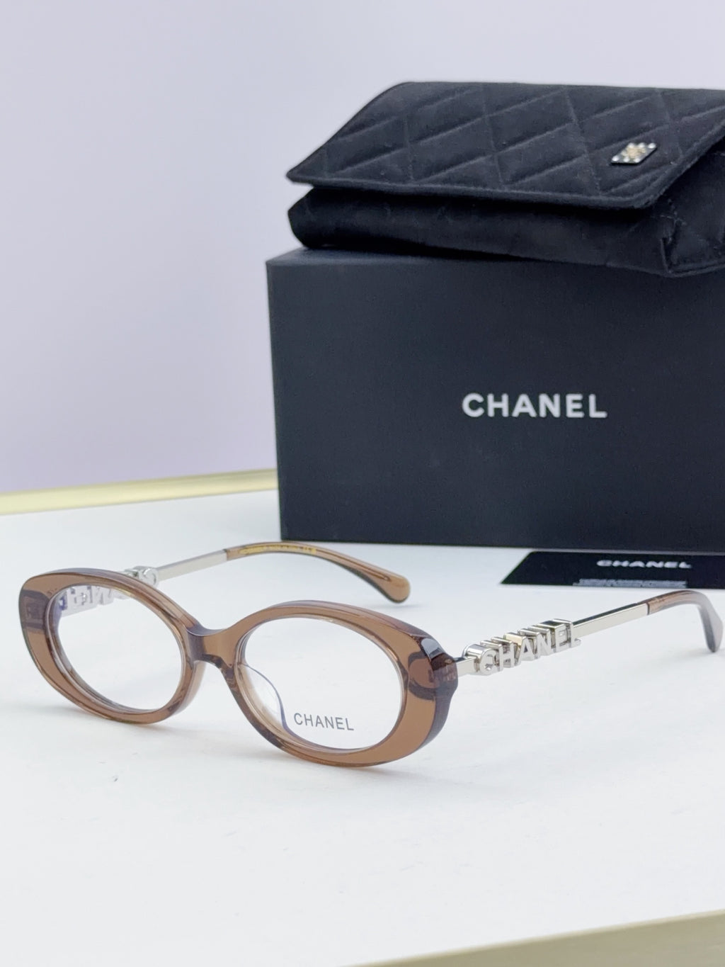 Chanel eyeglasses with light brown frame, gold-tone logo temples, and clear lenses; with case.
