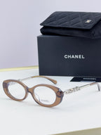Chanel eyeglasses with light brown frame, gold-tone logo temples, and clear lenses; with case.