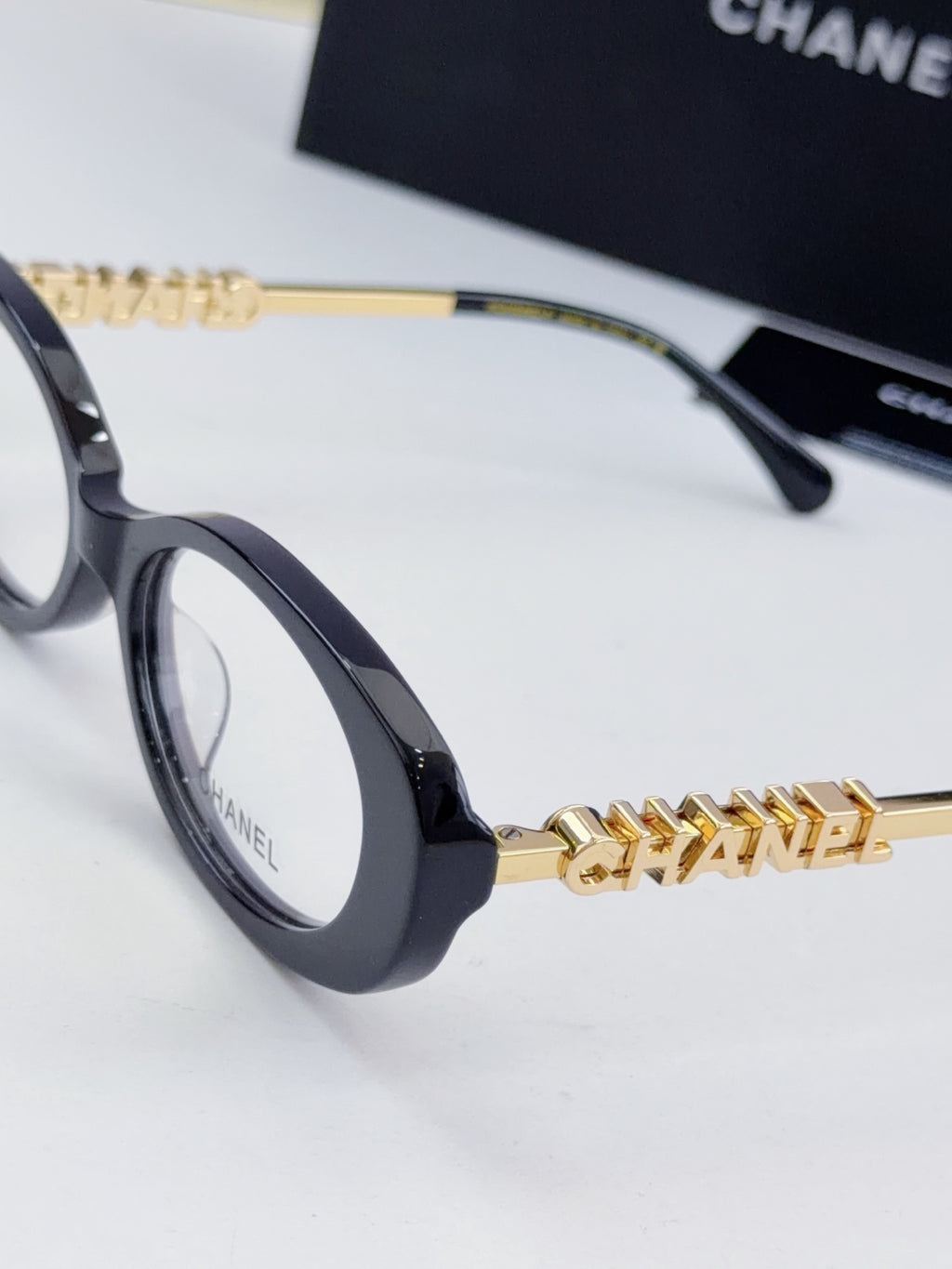 Chanel eyeglasses close-up: dark frame with gold-tone chain temple logo and round lenses.