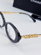 Chanel eyeglasses close-up: dark frame with gold-tone chain temple logo and round lenses.