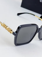Chanel square sunglasses close-up: dark frame, gold-tone logo chain temples, gray lenses