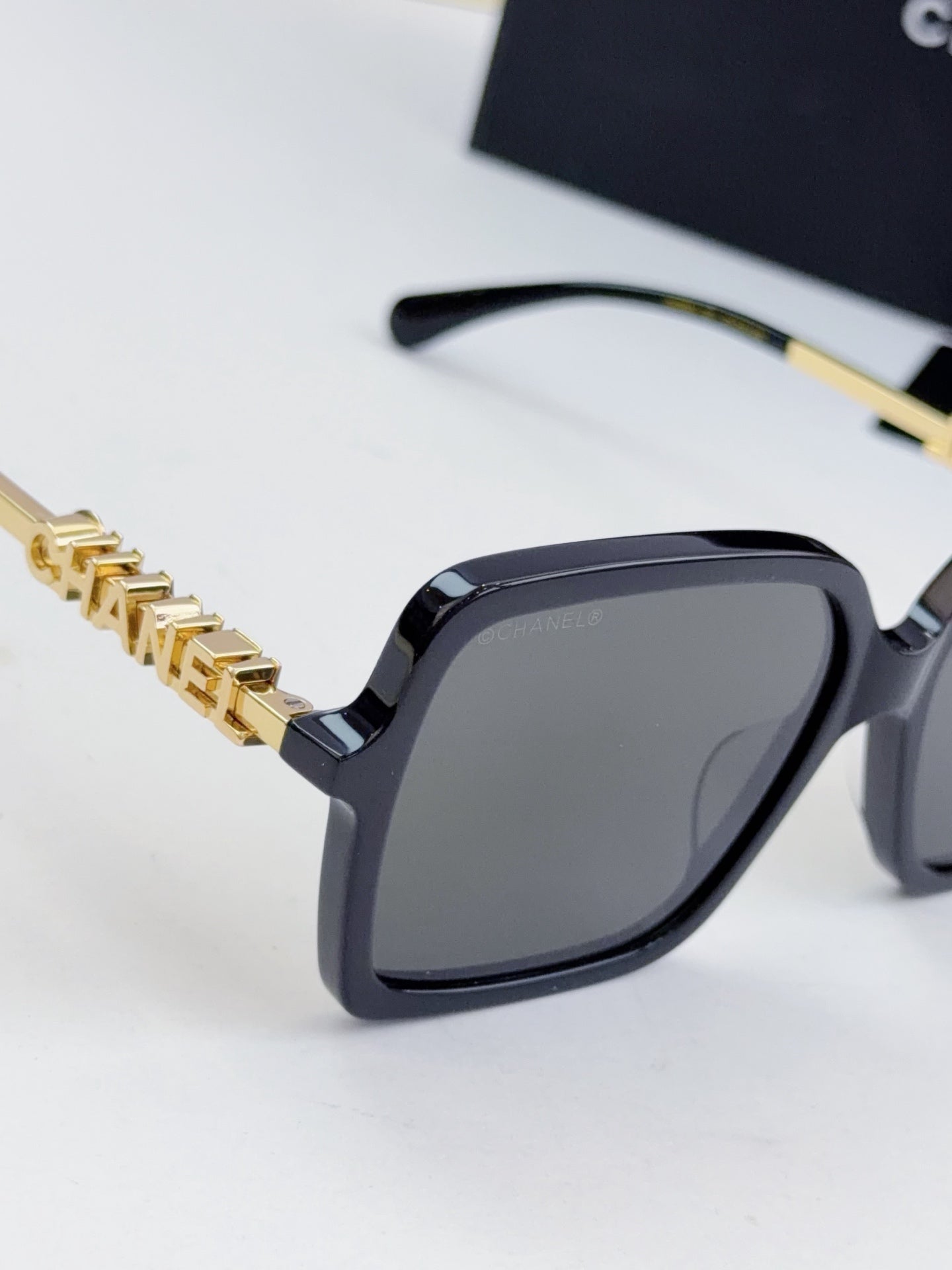 Chanel square sunglasses close-up: dark frame, gold-tone logo chain temples, gray lenses