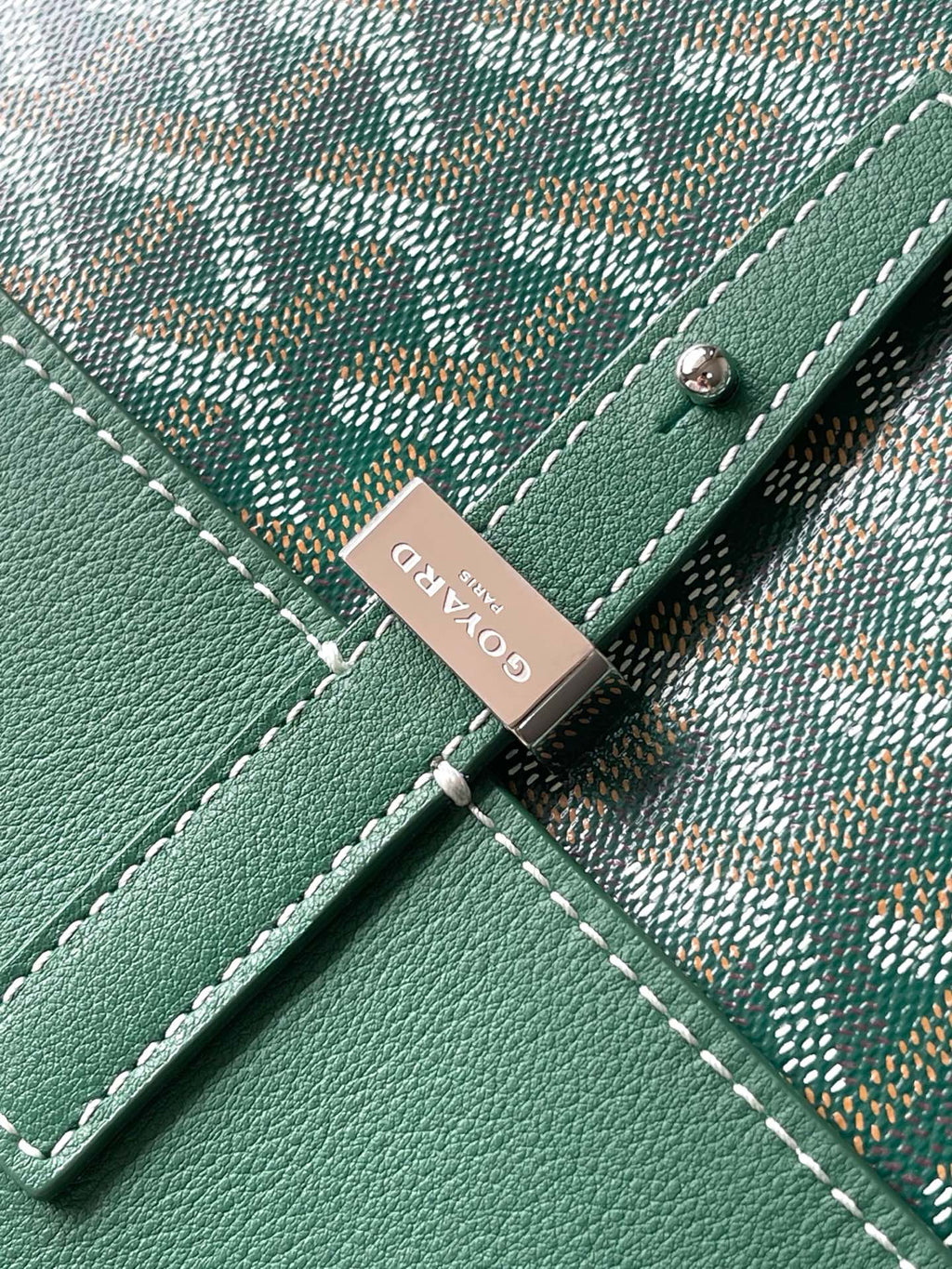 Green leather patch with metal tag and stitching on Goyard-pattern bag