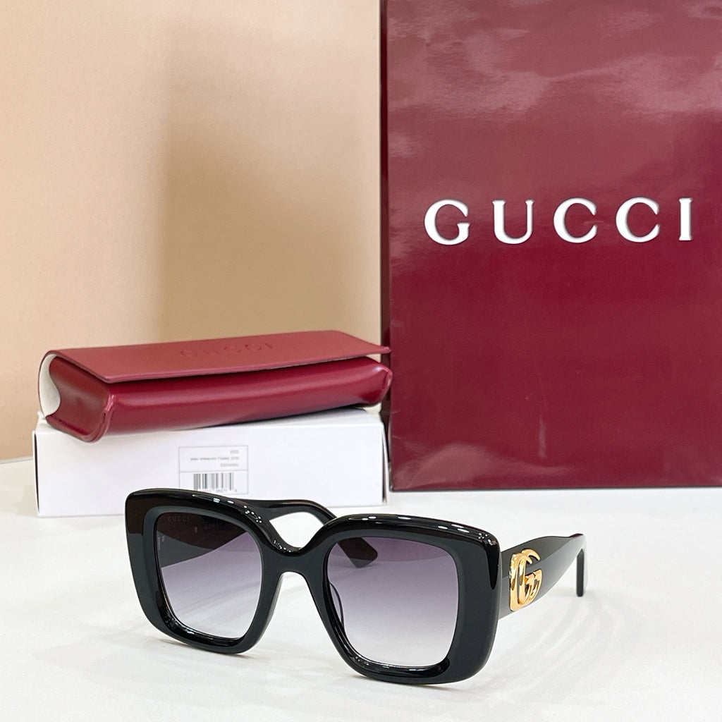 Gucci sunglasses with dark frames and tinted lenses, gold GG logo on the side.