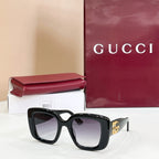 Gucci sunglasses with dark frames and tinted lenses, gold GG logo on the side.