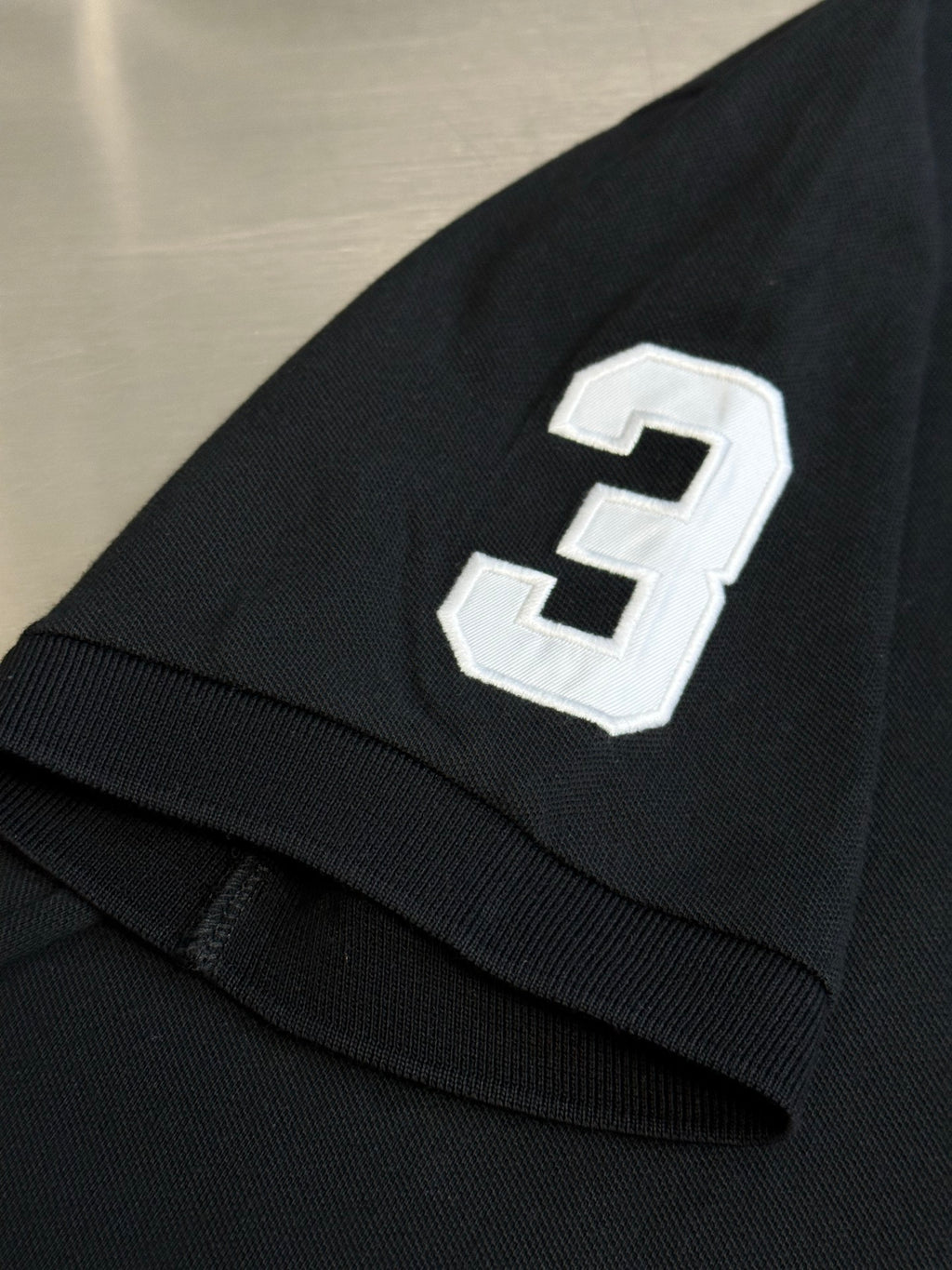 Dark navy polo shirt sleeve with white number 3 applique