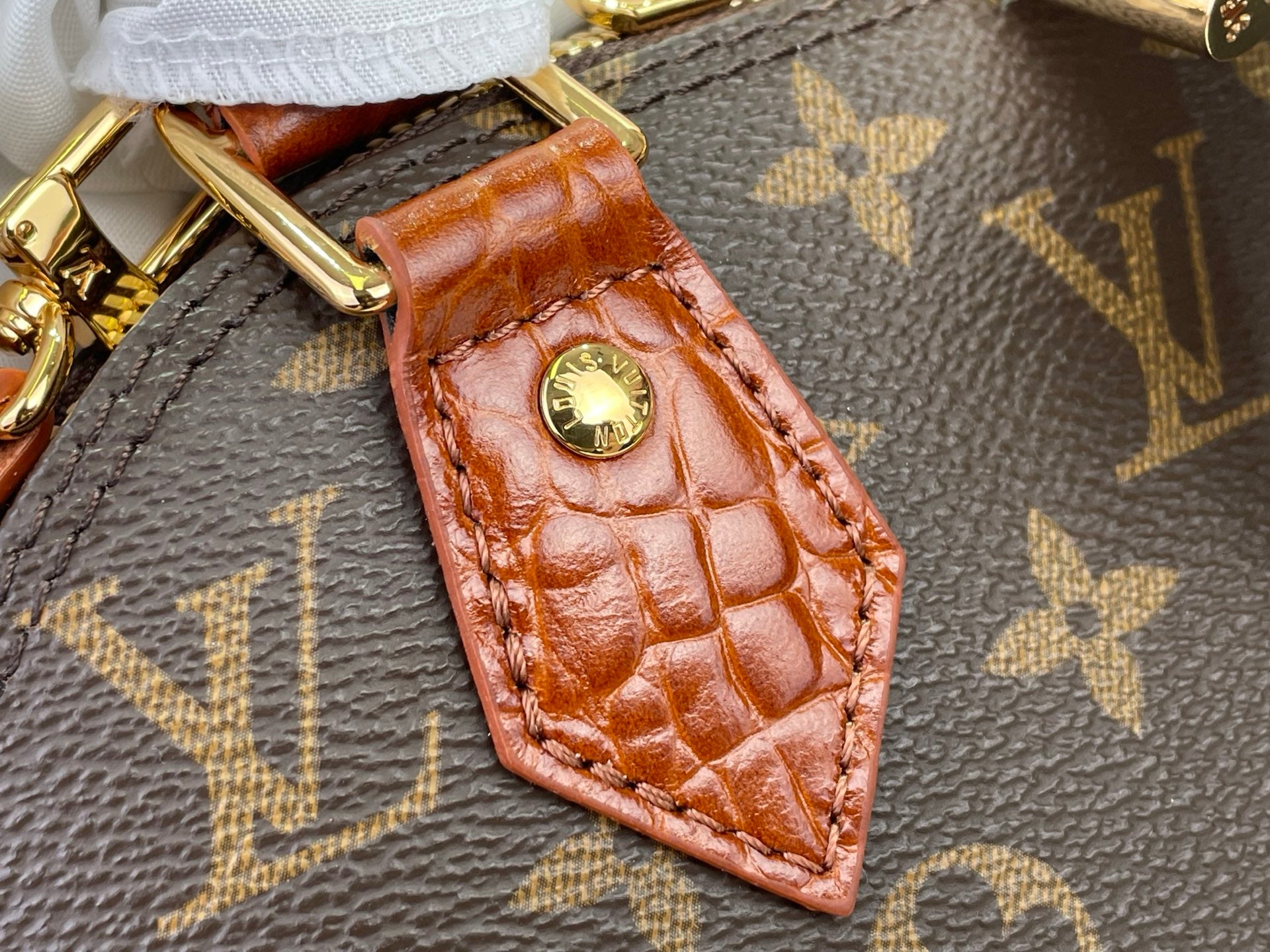 Louis Vuitton brown crocodile-style leather tag with gold stud on monogram bag