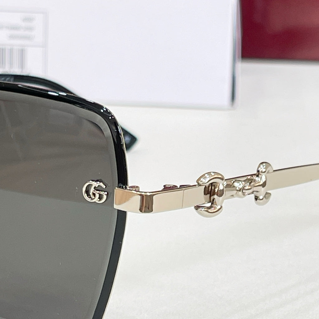 Gucci close-up of gold-tone hinge with GG emblem on black square sunglasses.
