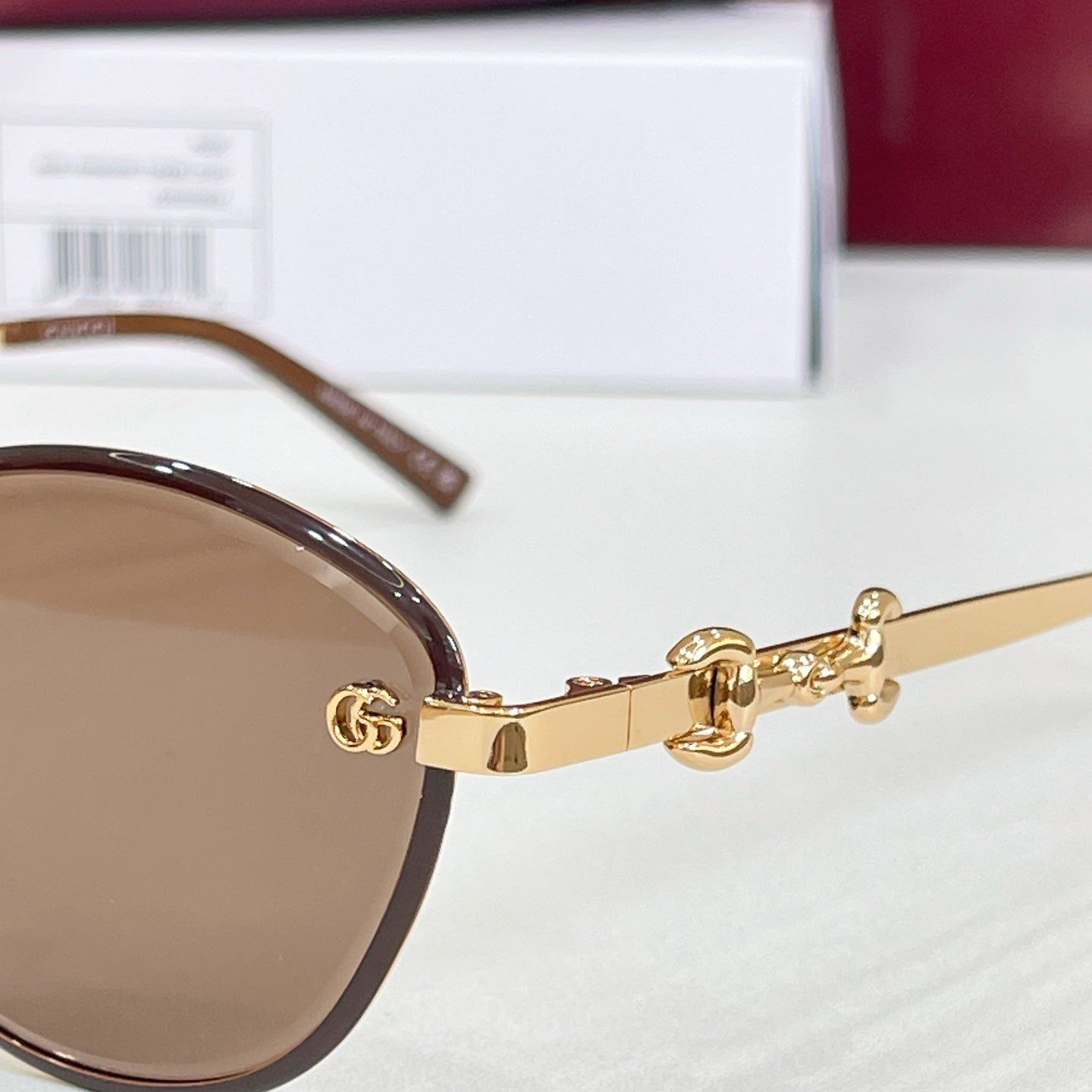 Gucci round sunglasses close-up: gold arms, brown lenses, logo charm at hinge