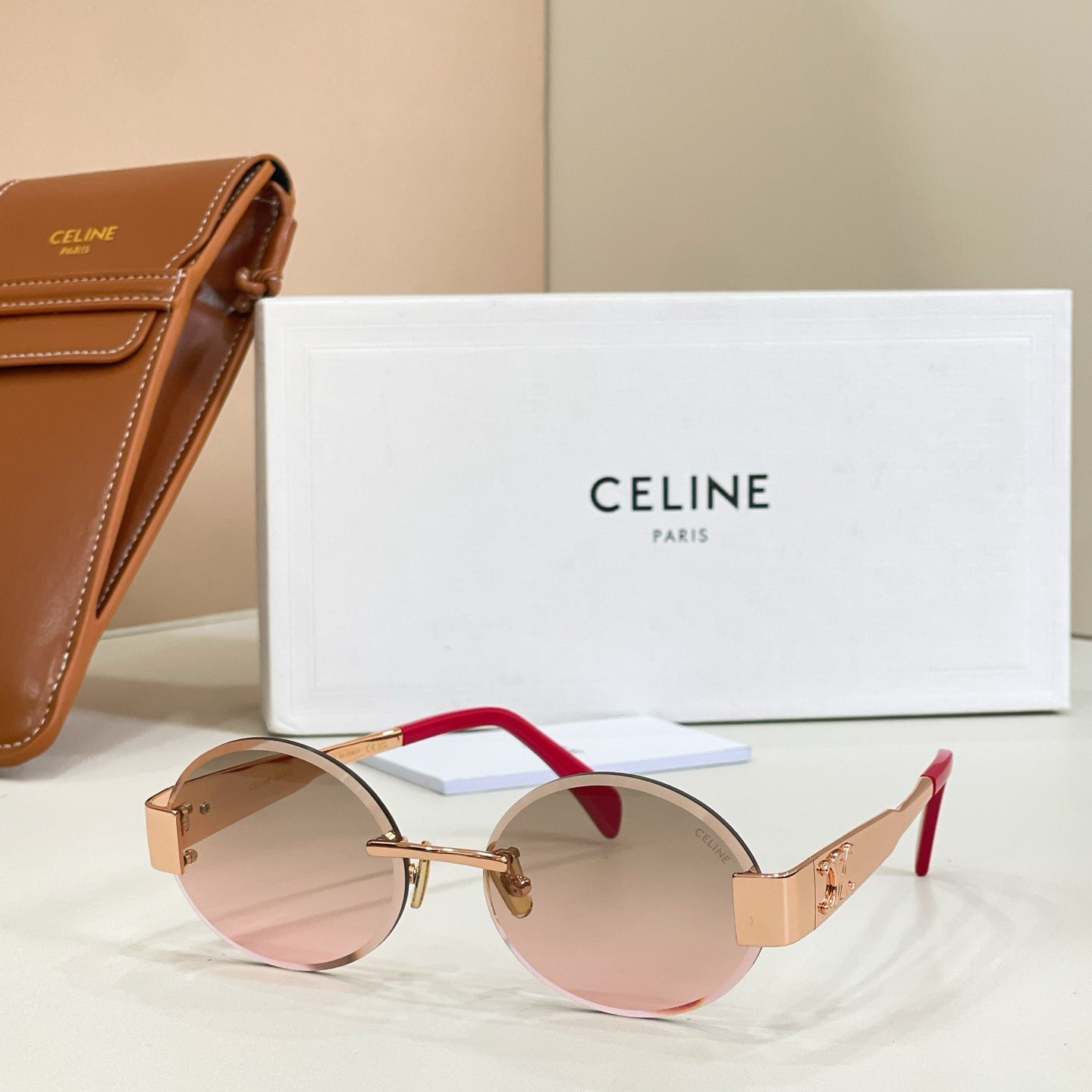 Gold-tone round sunglasses with rose-tinted lenses and red temple accents