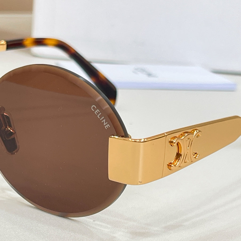 Close-up of gold-tone round sunglasses with brown lenses and engraved temple logo