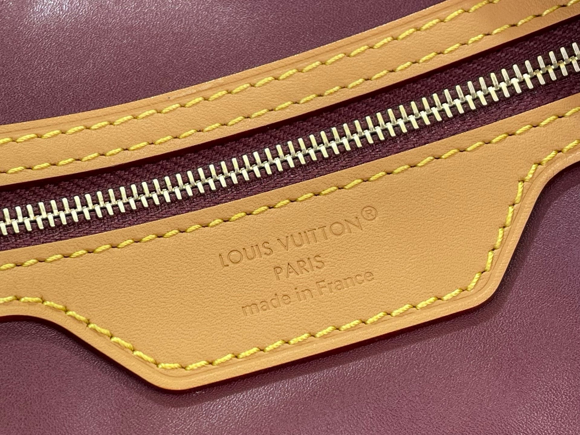 Louis Vuitton bag close-up of yellow trim, zipper, and embossed logo on leather