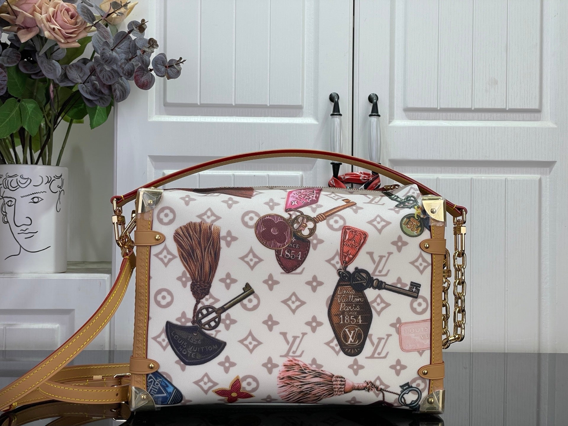 Monogram handbag with tan trim, gold-tone chain strap, and colorful patterned accents