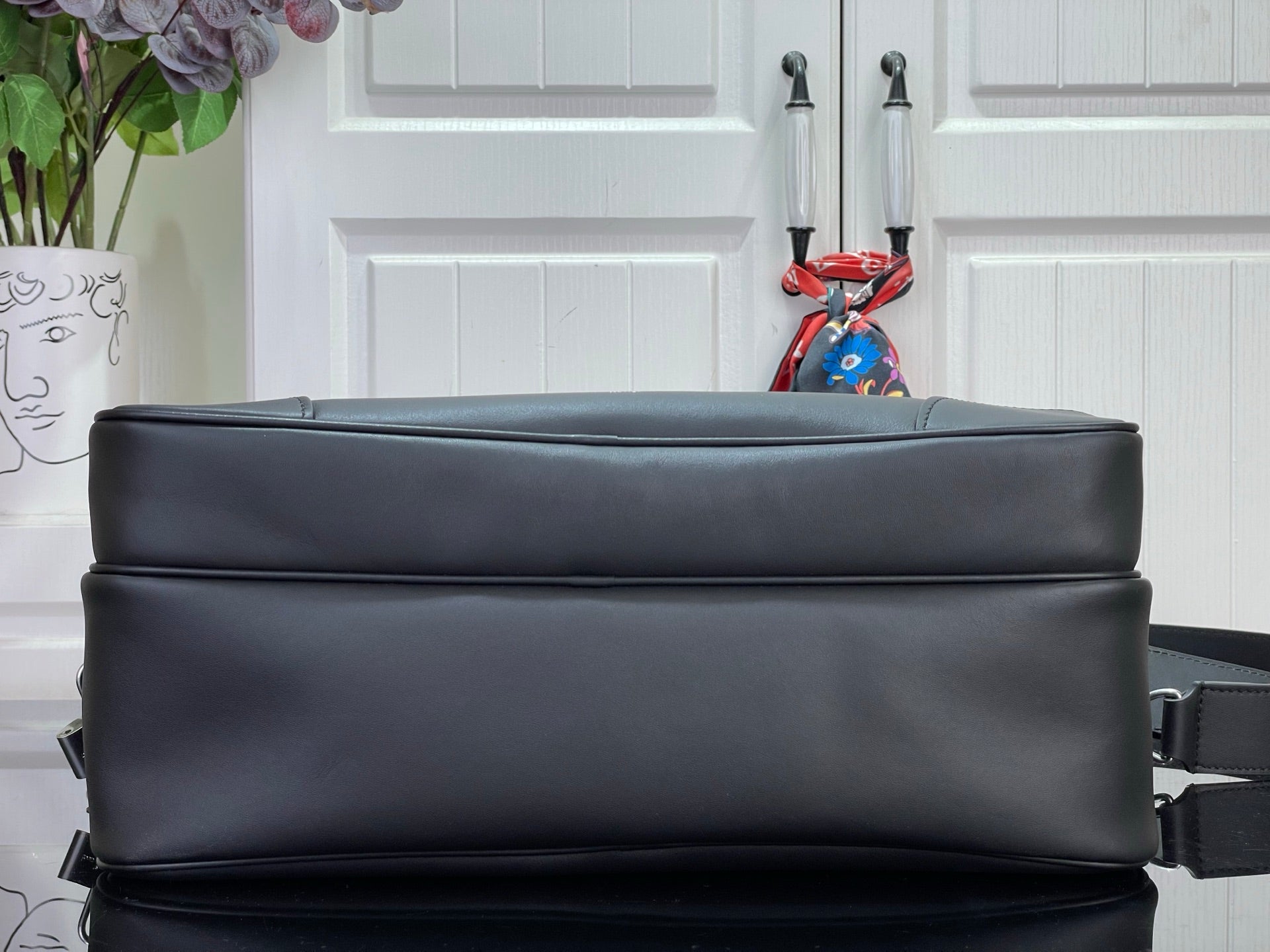 Dark leather crossbody bag with structured top edge and shoulder strap.