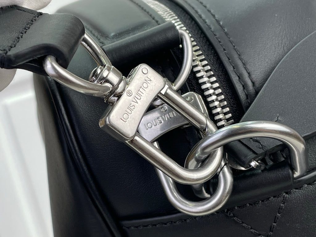 Dark leather bag detail with zip pull, metal rings, and embossed logo plates.