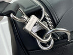 Dark leather bag detail with zip pull, metal rings, and embossed logo plates.