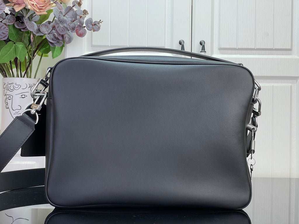 Dark leather crossbody bag with top zip and side metal hardware rings.