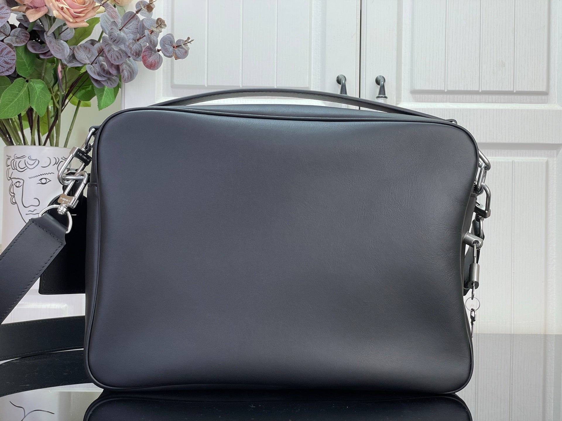 Dark leather crossbody bag with top zip and side metal hardware rings.