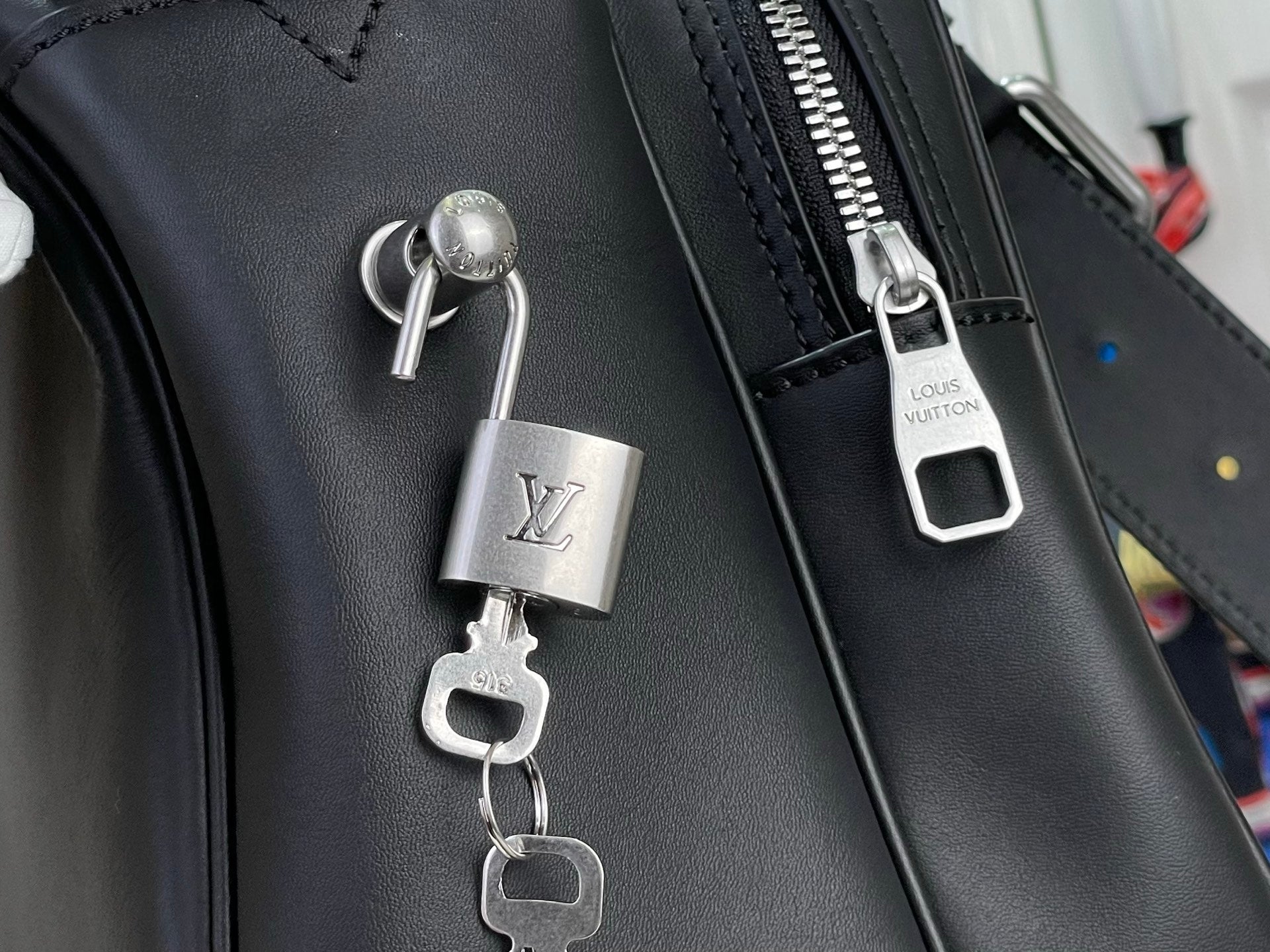 Louis Vuitton bag lock charm and metal zipper pull on dark leather