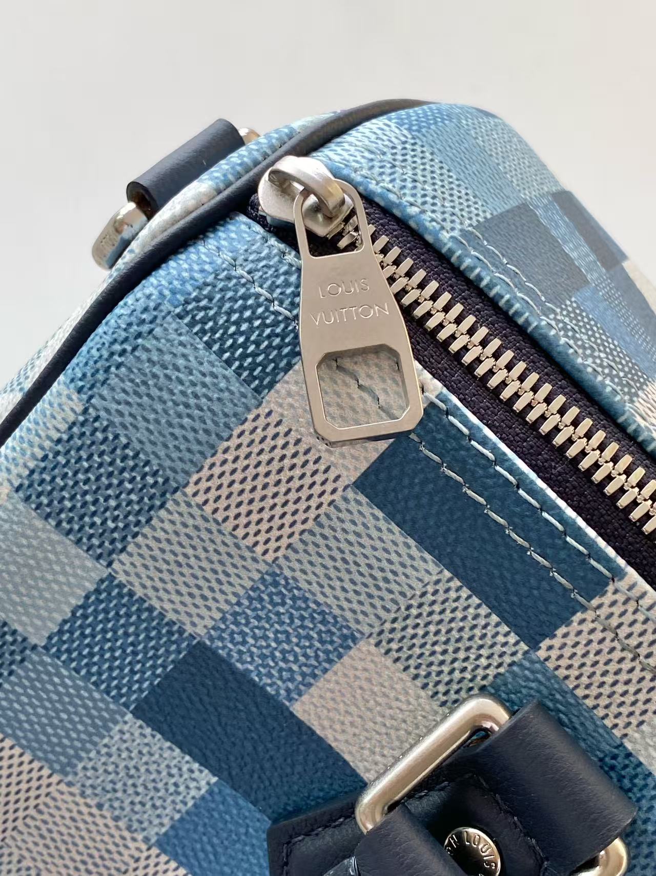 Blue checkered handbag corner with gold-tone zipper pull and leather strap