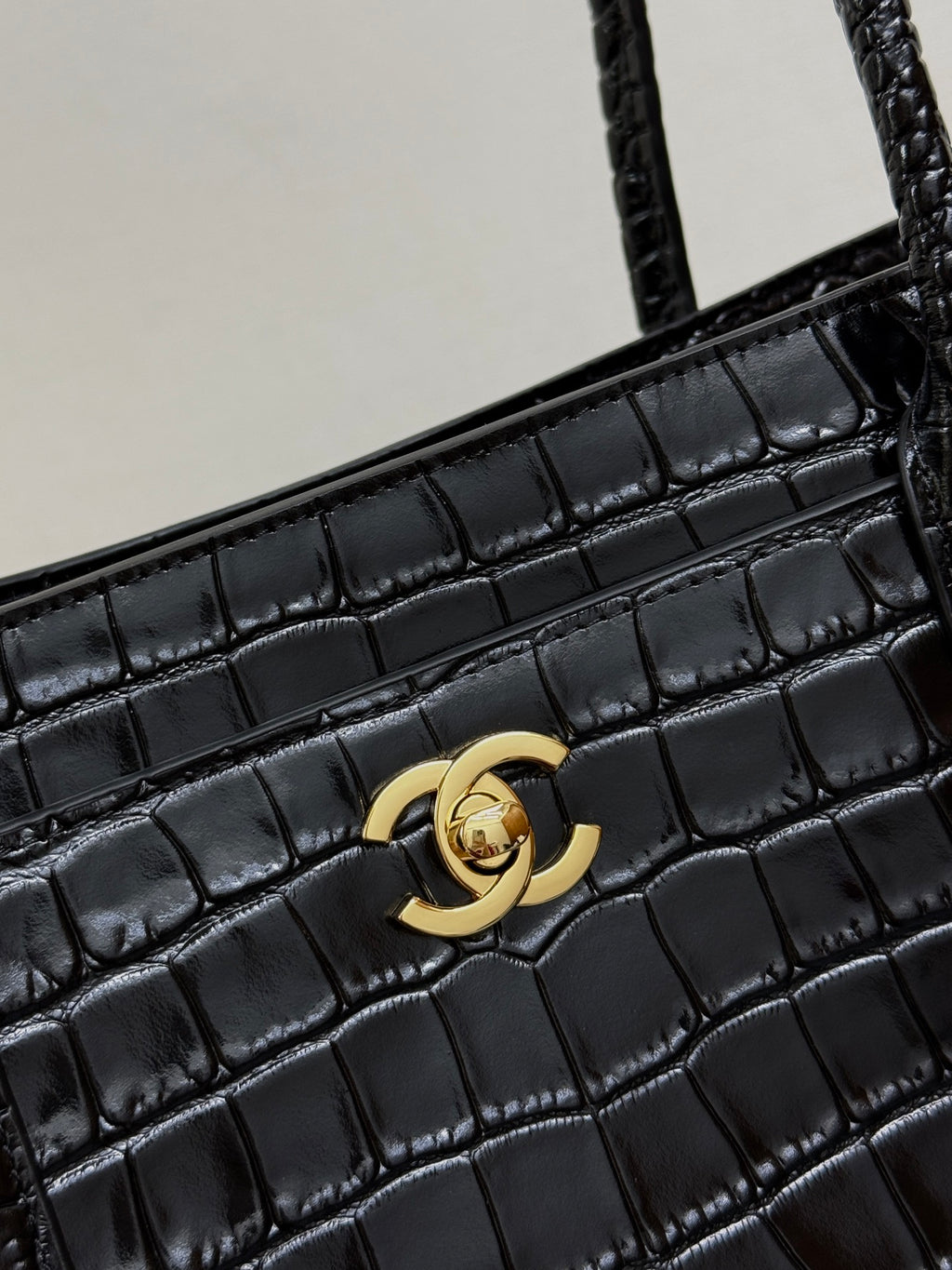 Gold Chanel CC clasp on black croc-texture bag front