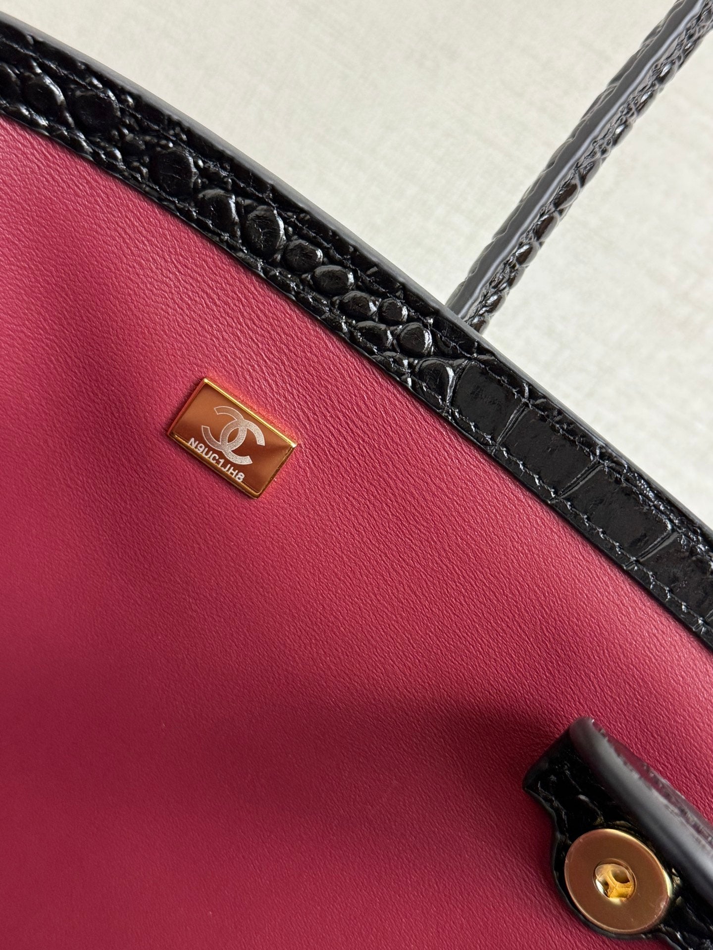 Black croc-texture bag exterior with gold logo plate and round button snap