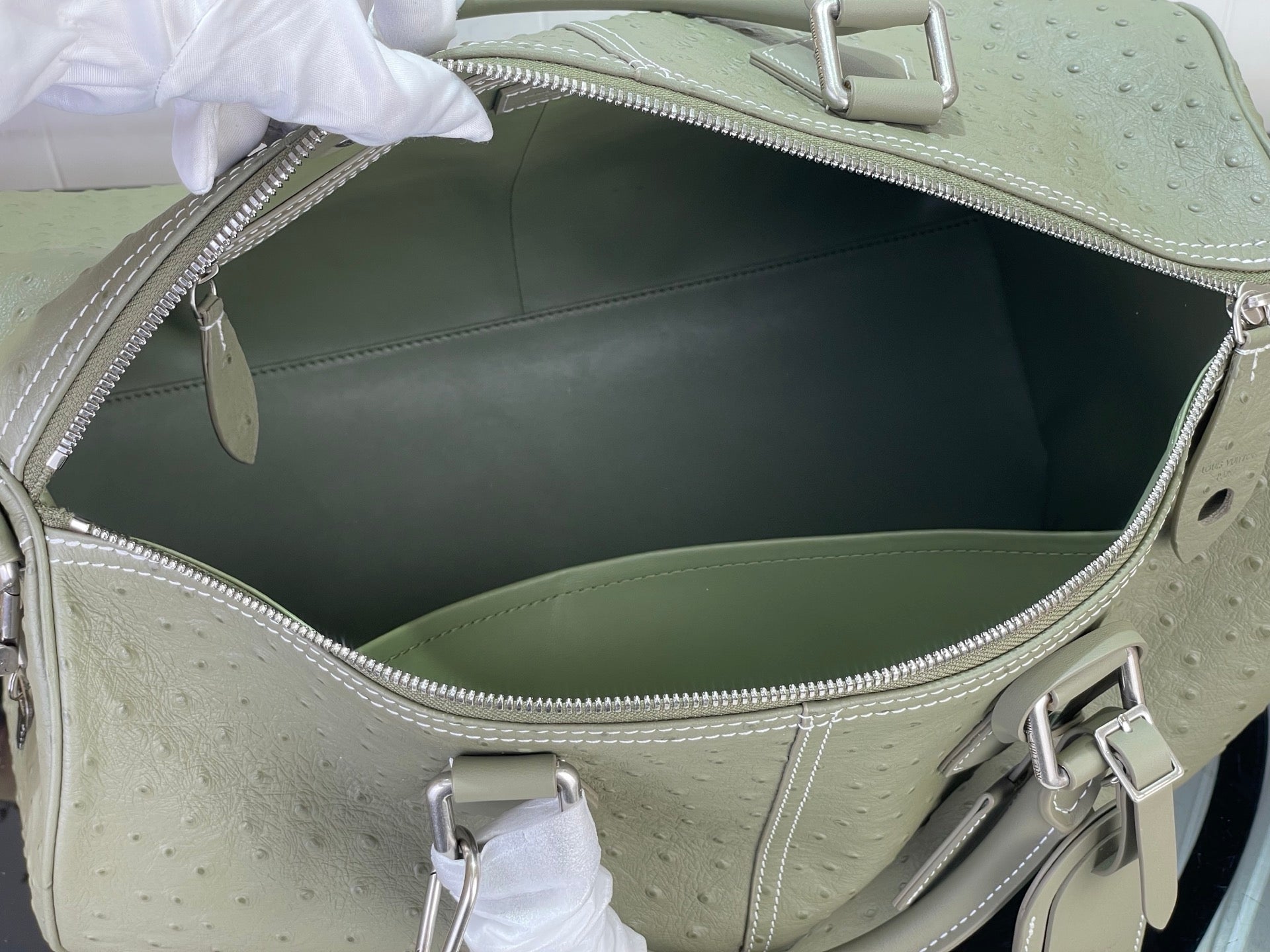 Open sage green Louis Vuitton bag interior with metal clasp and lining