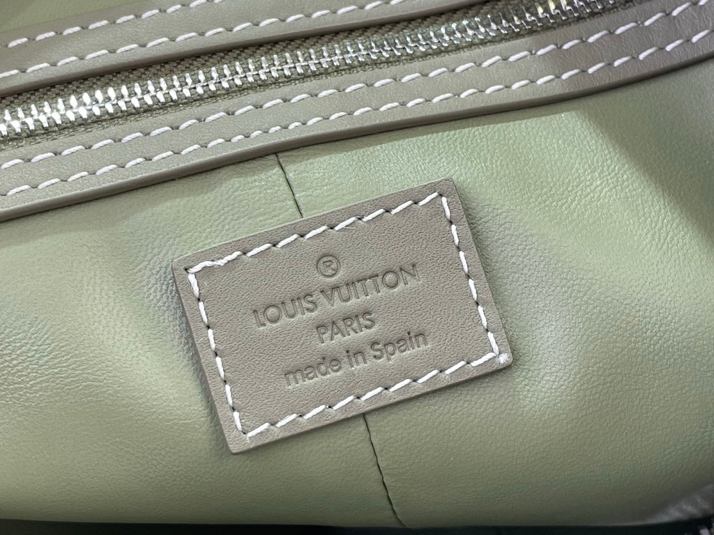 Sage green Louis Vuitton logo label with visible stitching on leather panel