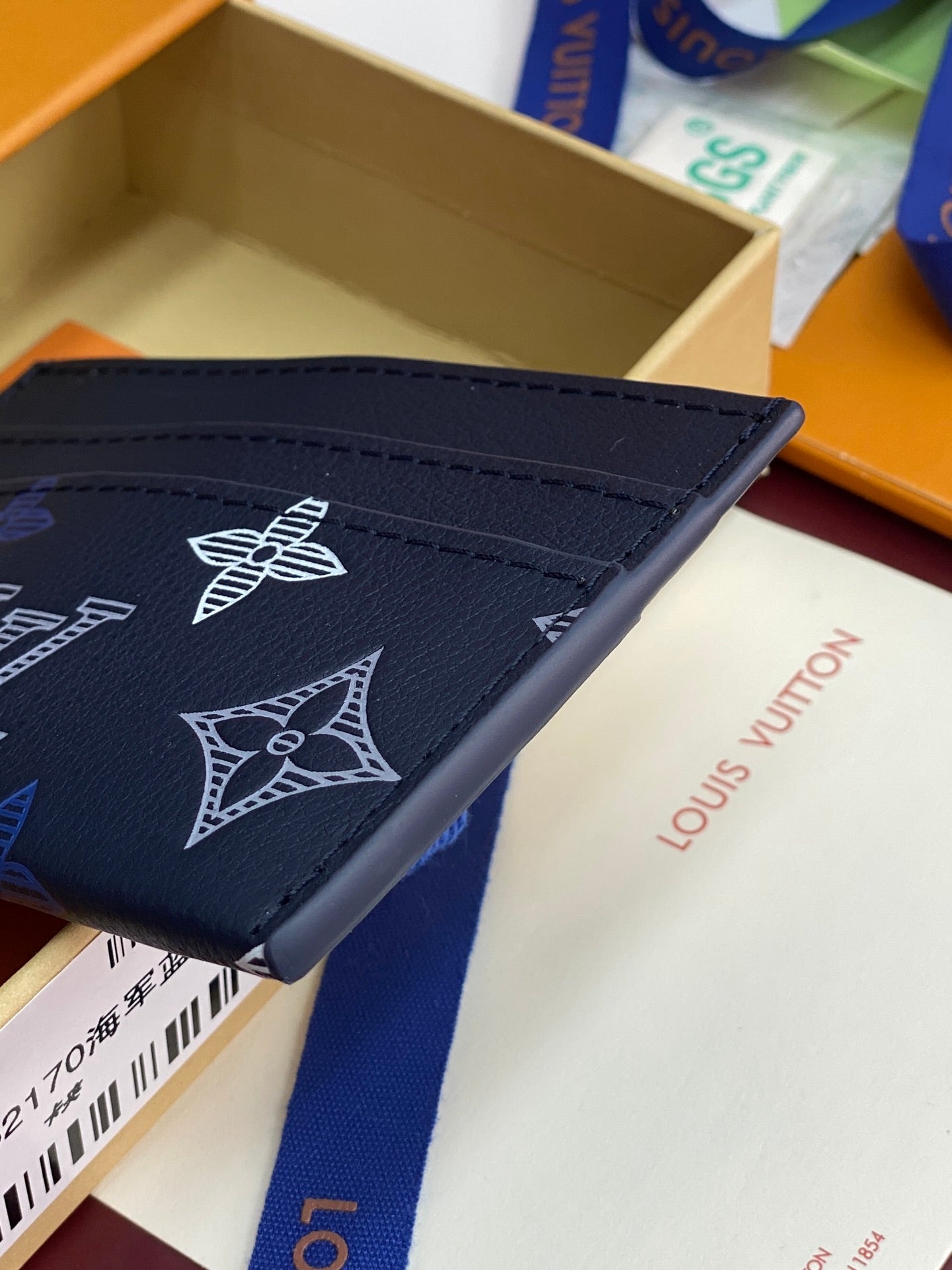 Small navy wallet corner with logo pattern and top stitched flap edge.