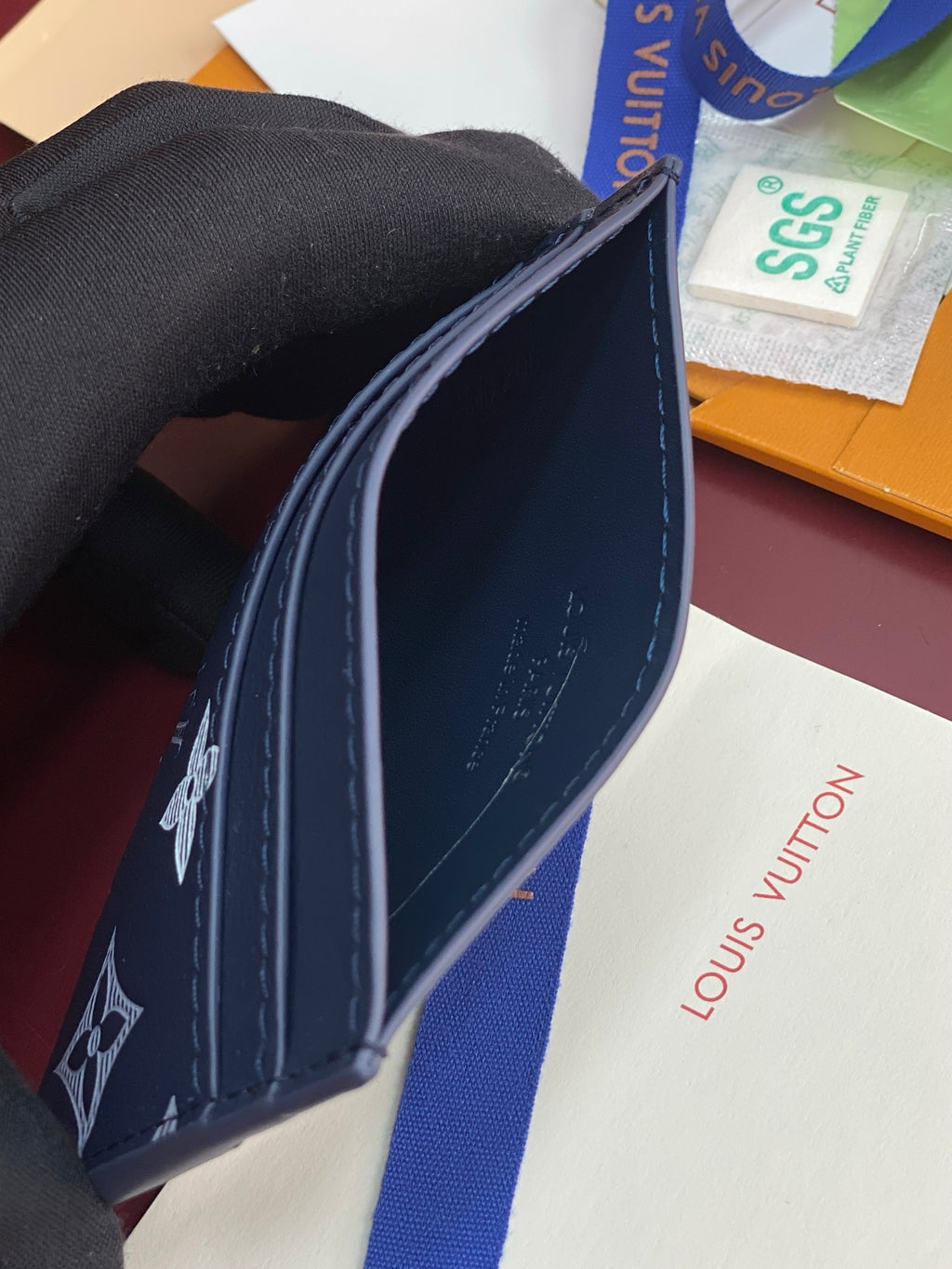 Small navy wallet side view with contrast stitching and printed logo motifs.