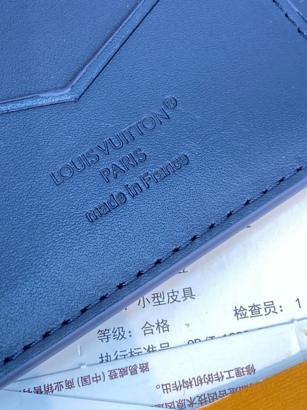 Louis Vuitton small card wallet close-up, embossed 'LOUIS VUITTON' on blue leather