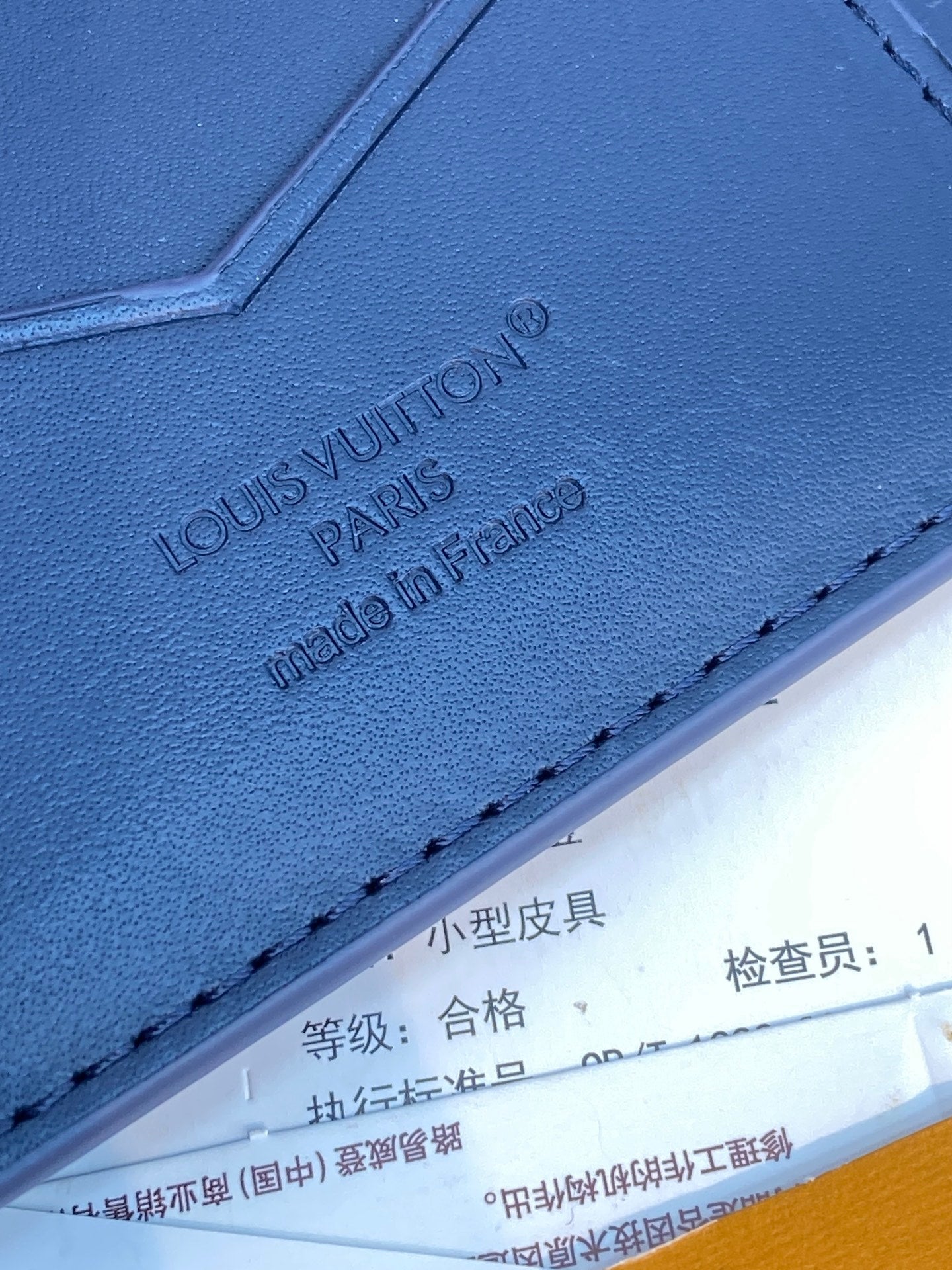 Louis Vuitton small card wallet close-up, embossed 'LOUIS VUITTON' on blue leather