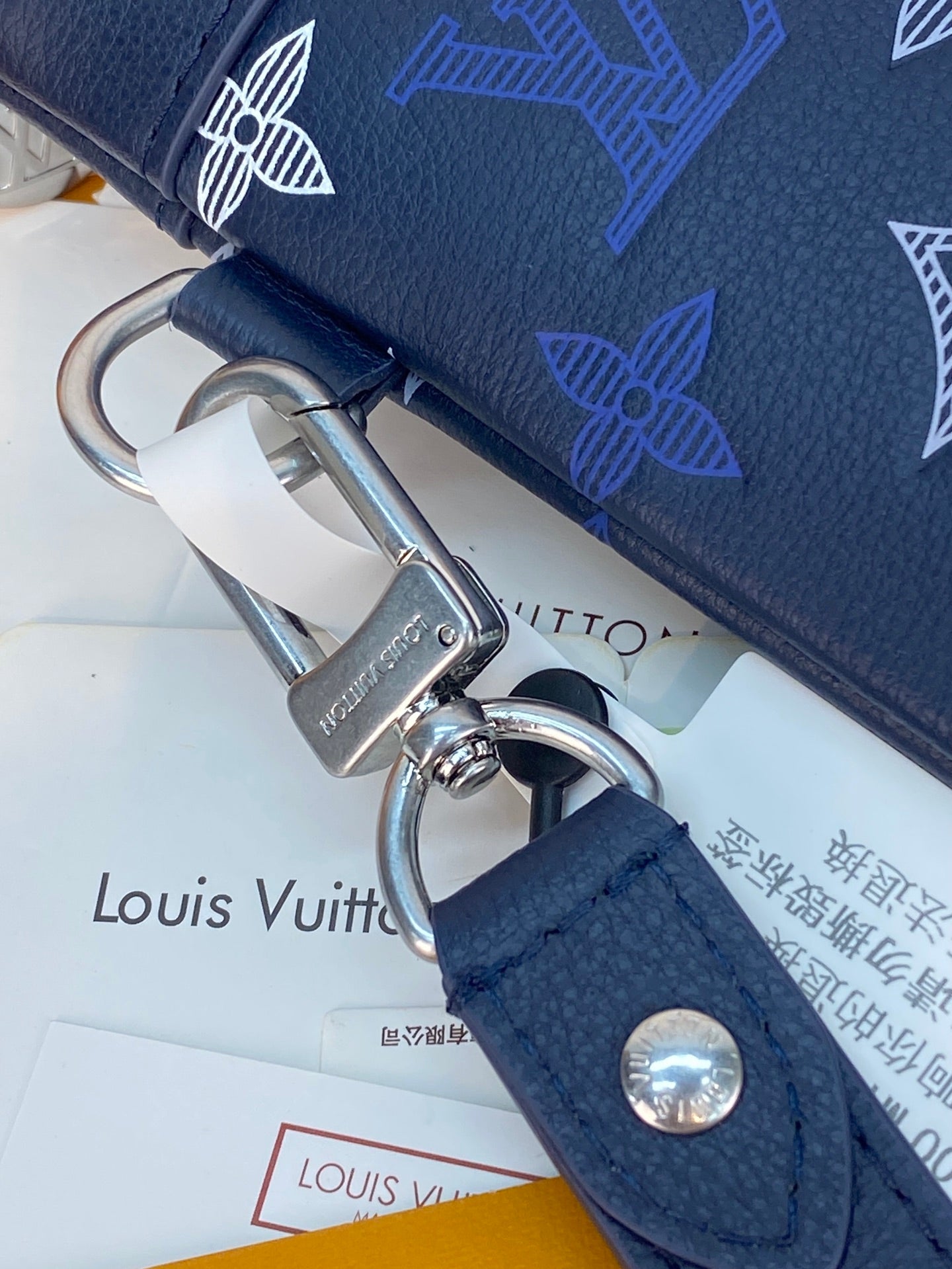 Blue Louis Vuitton small bag close-up of strap loop with metal ring and snap button.