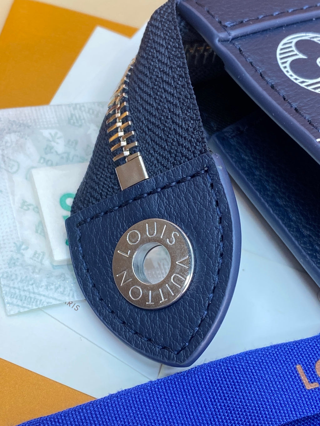 Blue leather snap detail with round logo plate and gold-tone rivet