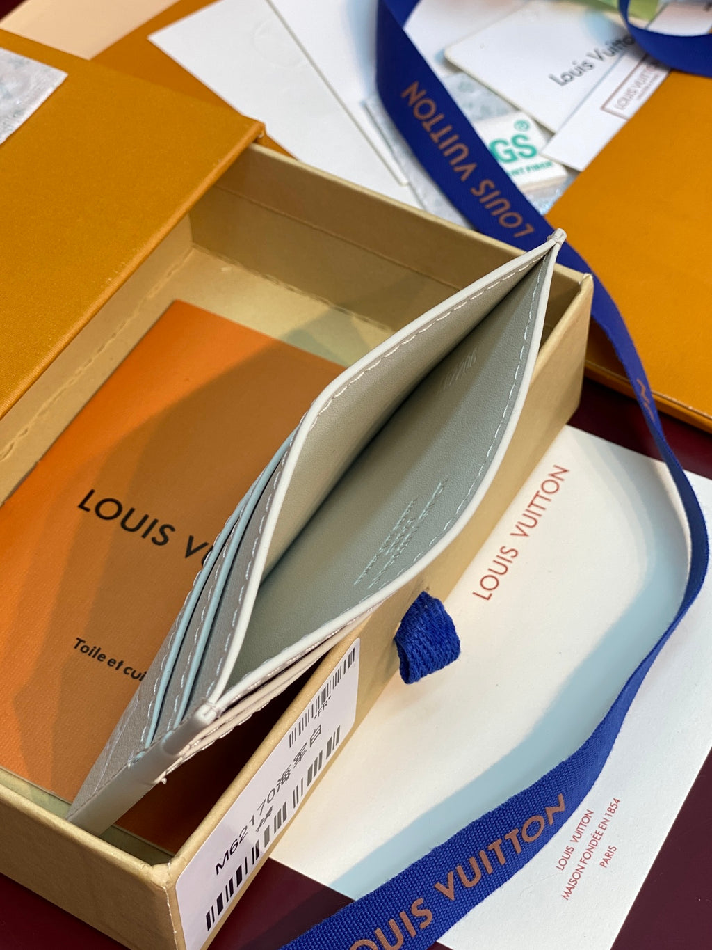 Louis Vuitton card holder in light cream with blue and dark monogram pattern, shown partly open