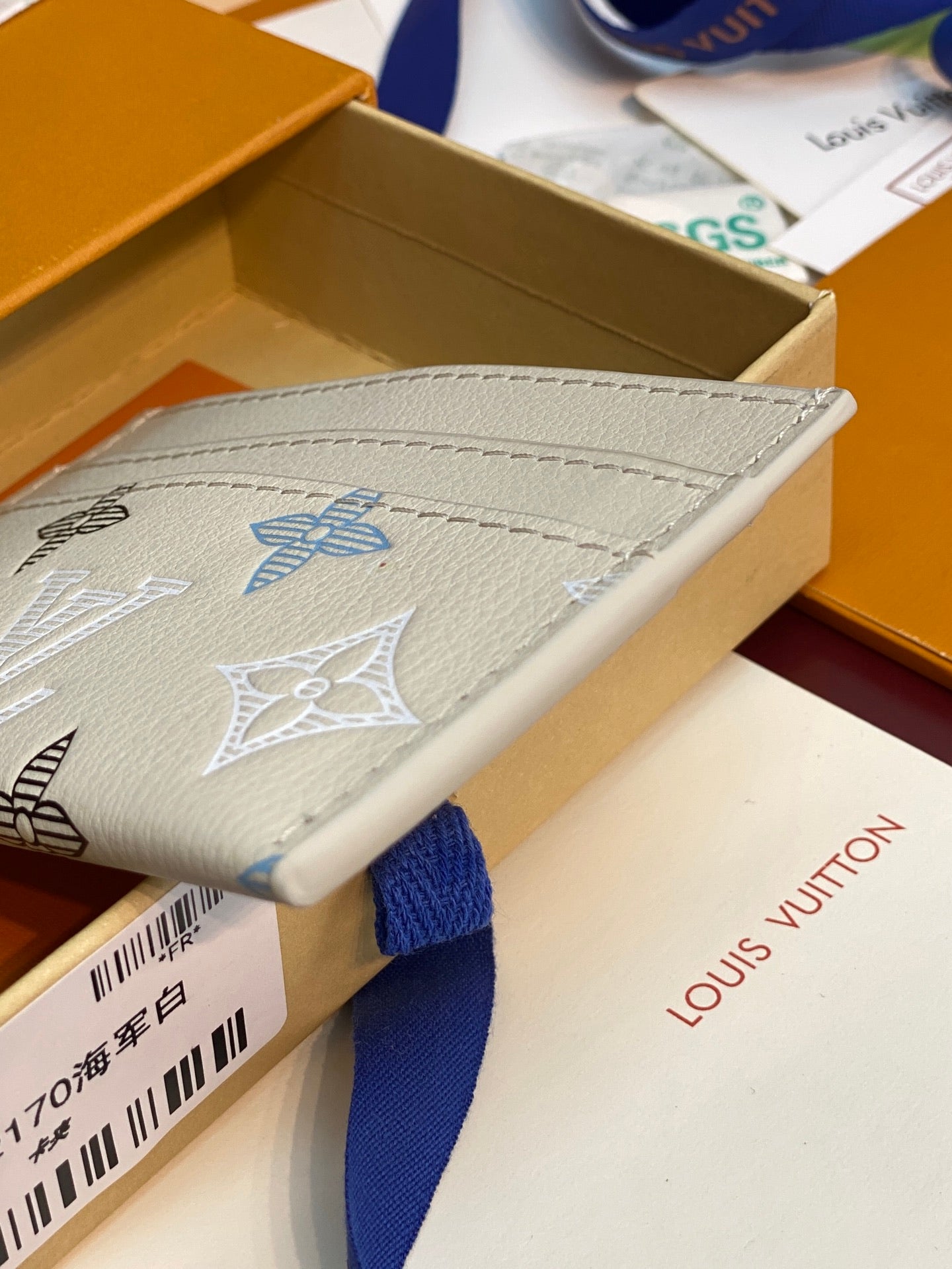 Louis Vuitton card holder in light cream with blue and dark monogram pattern, top edge visible