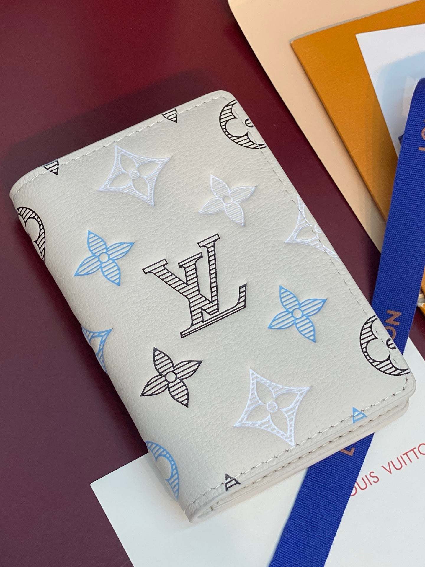 Men's Louis Vuitton small card wallet, angled view of white with blue and black monogram pattern.