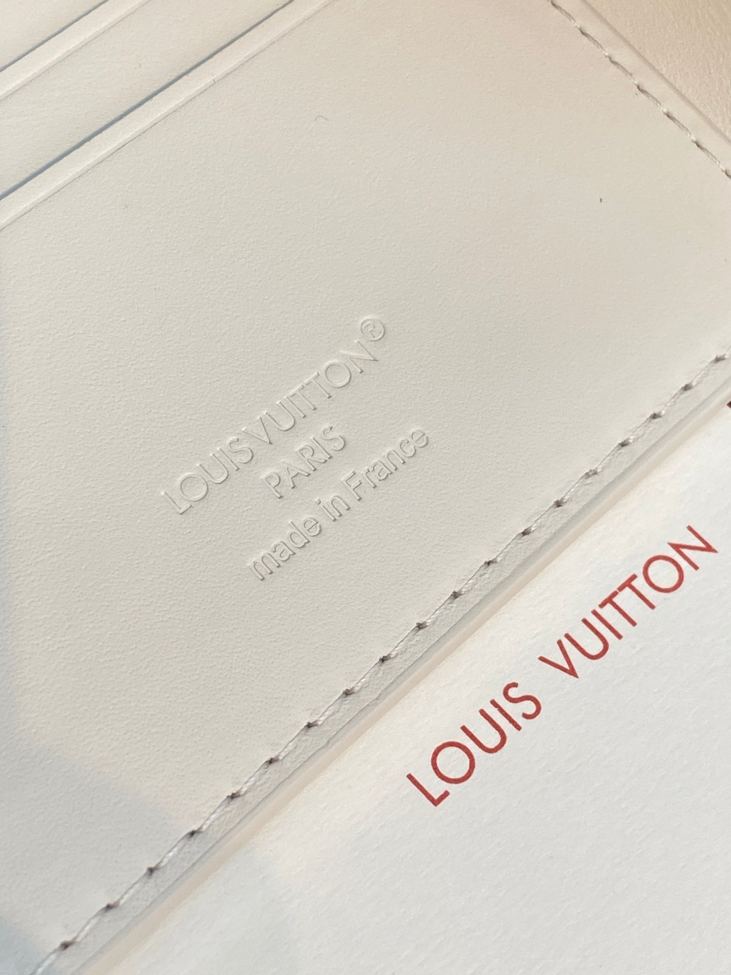 Louis Vuitton wallet close-up of embossed logo and stitching on white leather.