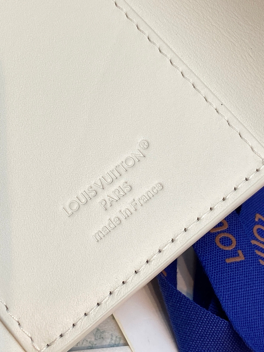 White leather card case with embossed Louis Vuitton text and stitched edge seam