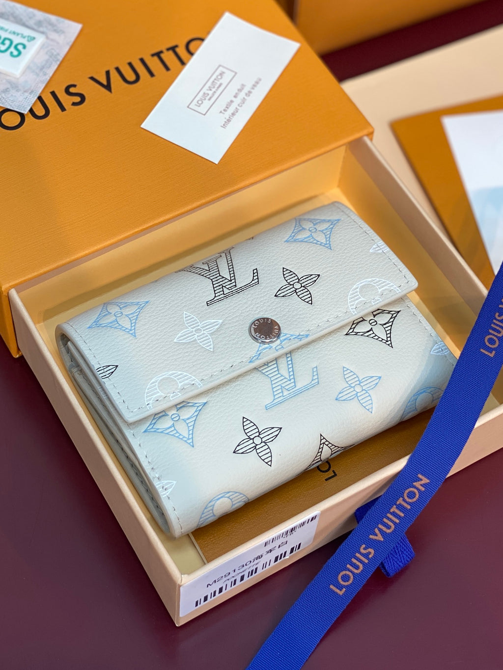White small wallet with blue monogram print and round snap button, flap view