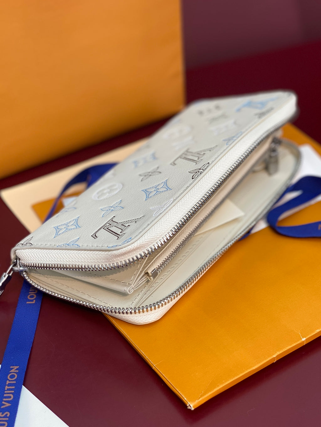 Small zip wallet with white leather and blue monogram pattern, front angle.