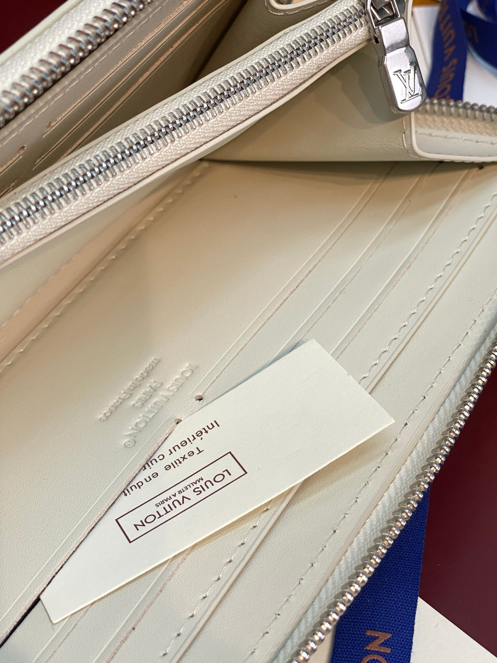 Interior of small zip wallet with pale leather, stitching detail, and brand tag.