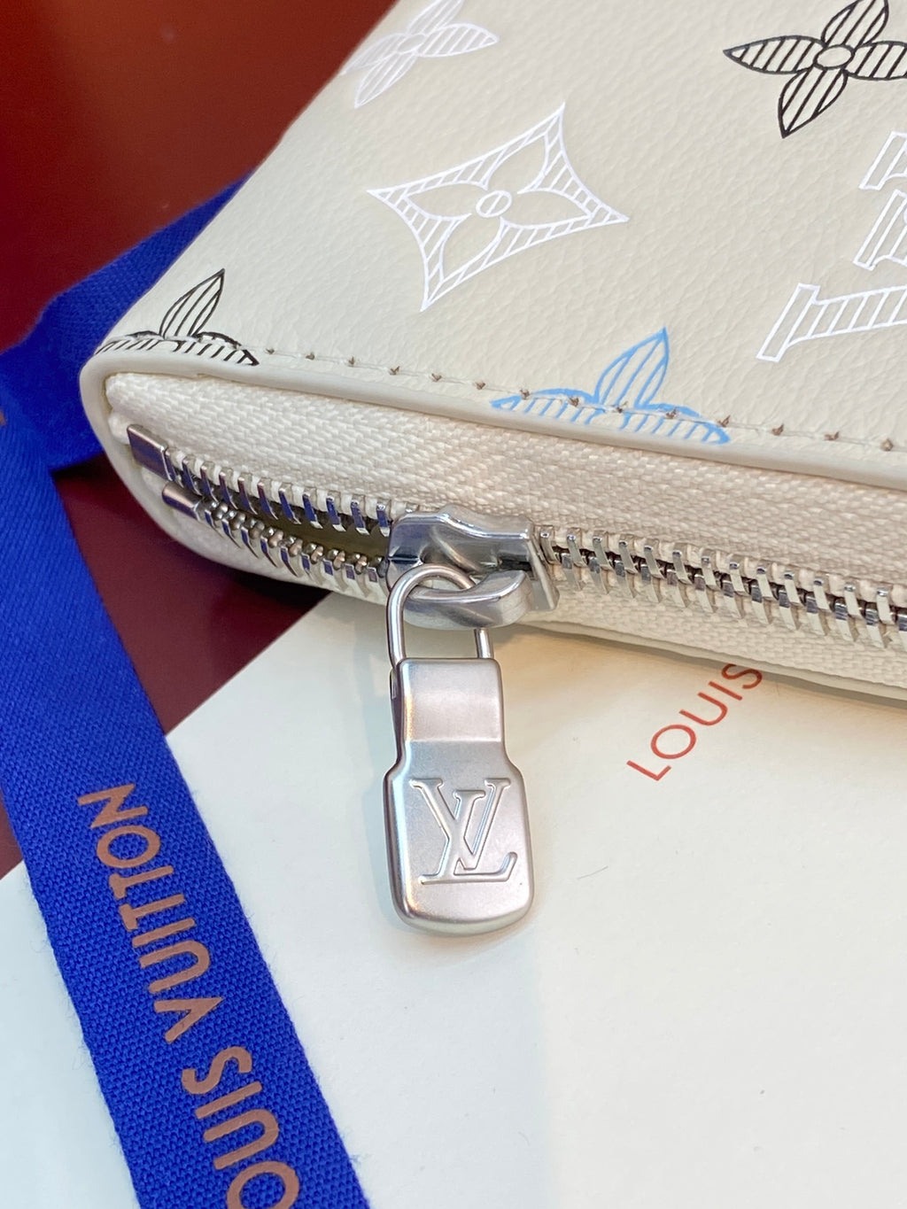 Small zip wallet corner close-up with silver zipper pull and Louis Vuitton charm.