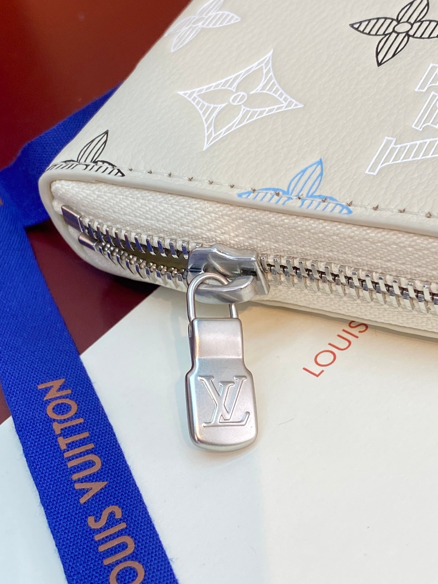 Small zip wallet corner close-up with silver zipper pull and Louis Vuitton charm.