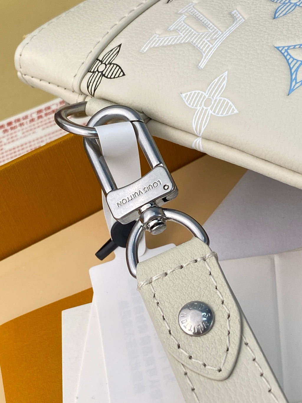 Key-ring attachment and silver clasp on white monogram clutch with stitched leather tab.