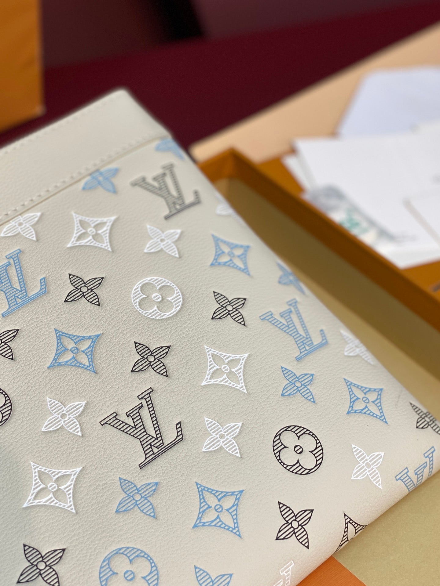 Close-up of white clutch bag with blue and black monogram motifs.