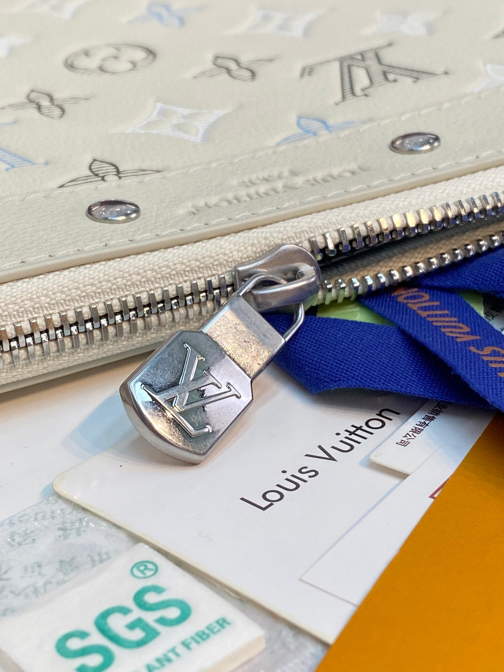 Louis Vuitton bag zipper pull with LV logo, on light beige canvas