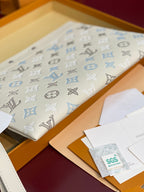 White monogram zip clutch with blue motifs, folded in a box with papers and tags.