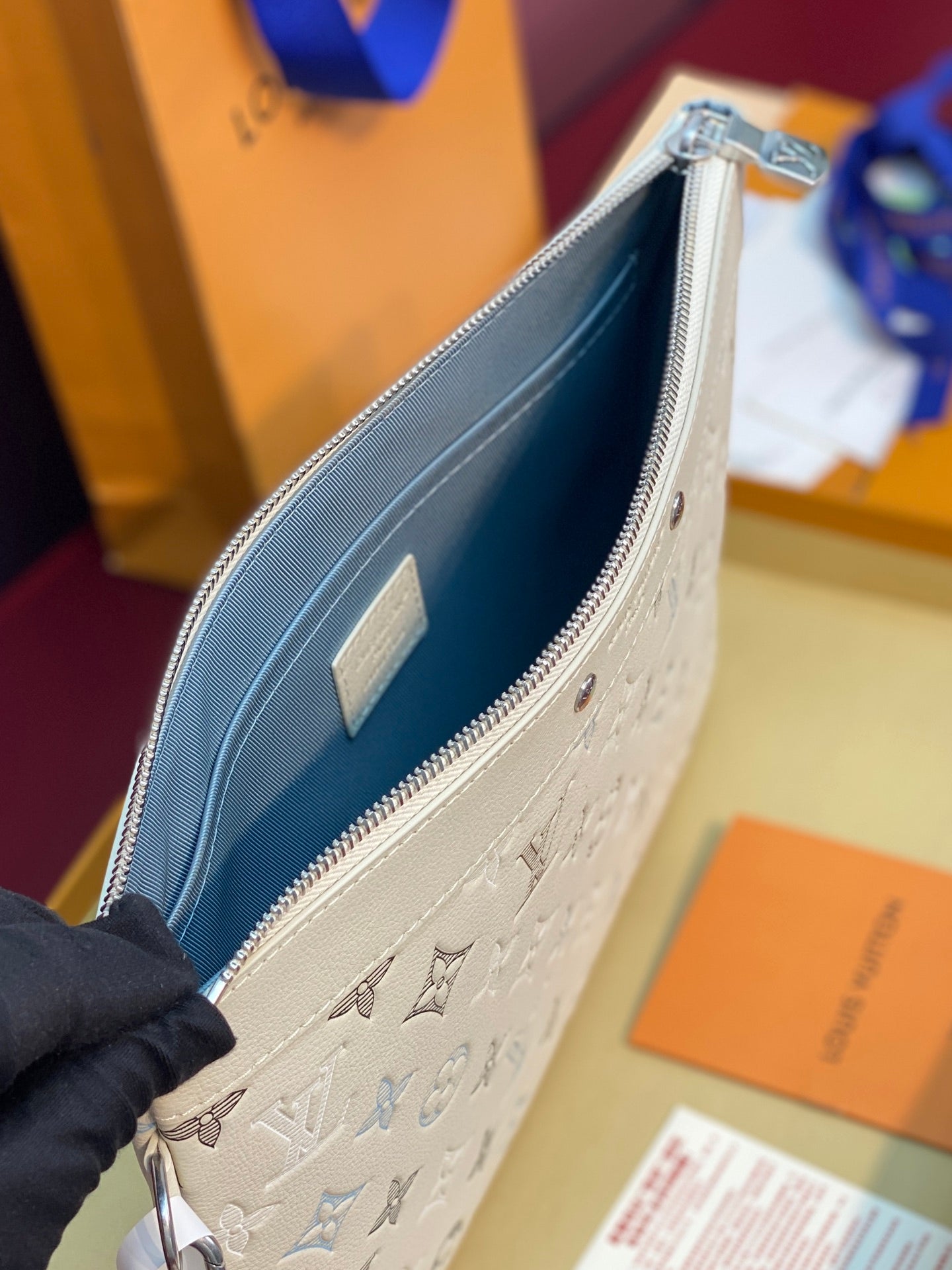 Side view of small monogram zip clutch in white with silver zipper and blue fabric lining.