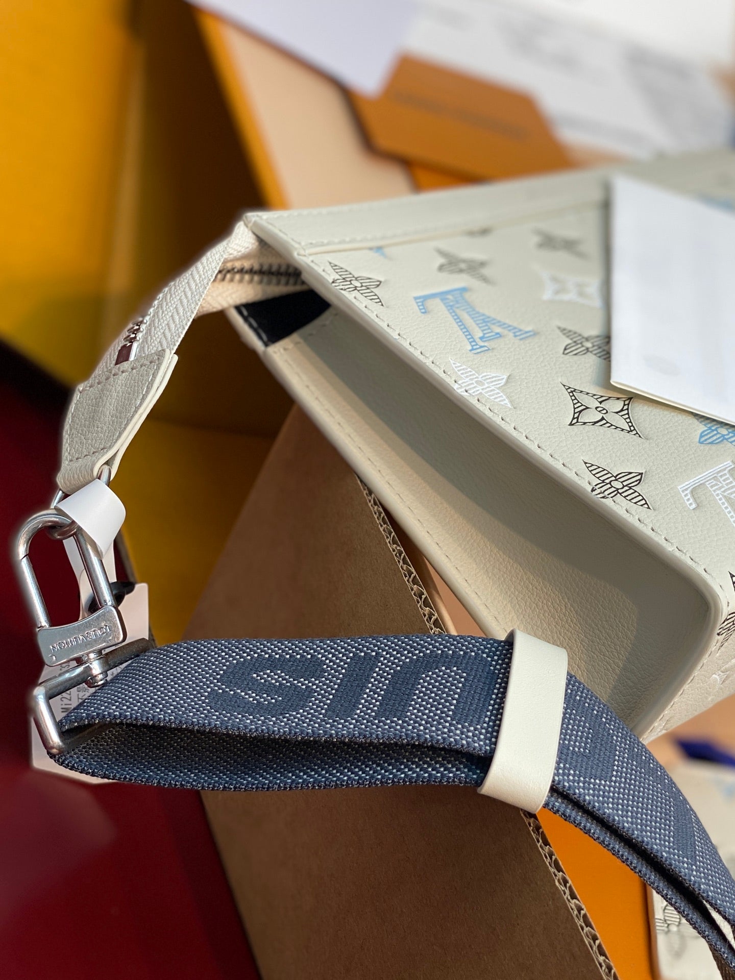 Cream monogram shoulder bag with navy strap and silver carabiner clasp, side view